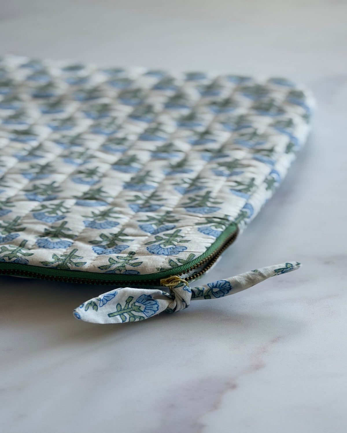 Close-up of the Blue Blossom hand block printed cotton fabric, quilted stitching and the contrast green zipper with bow tie detail.