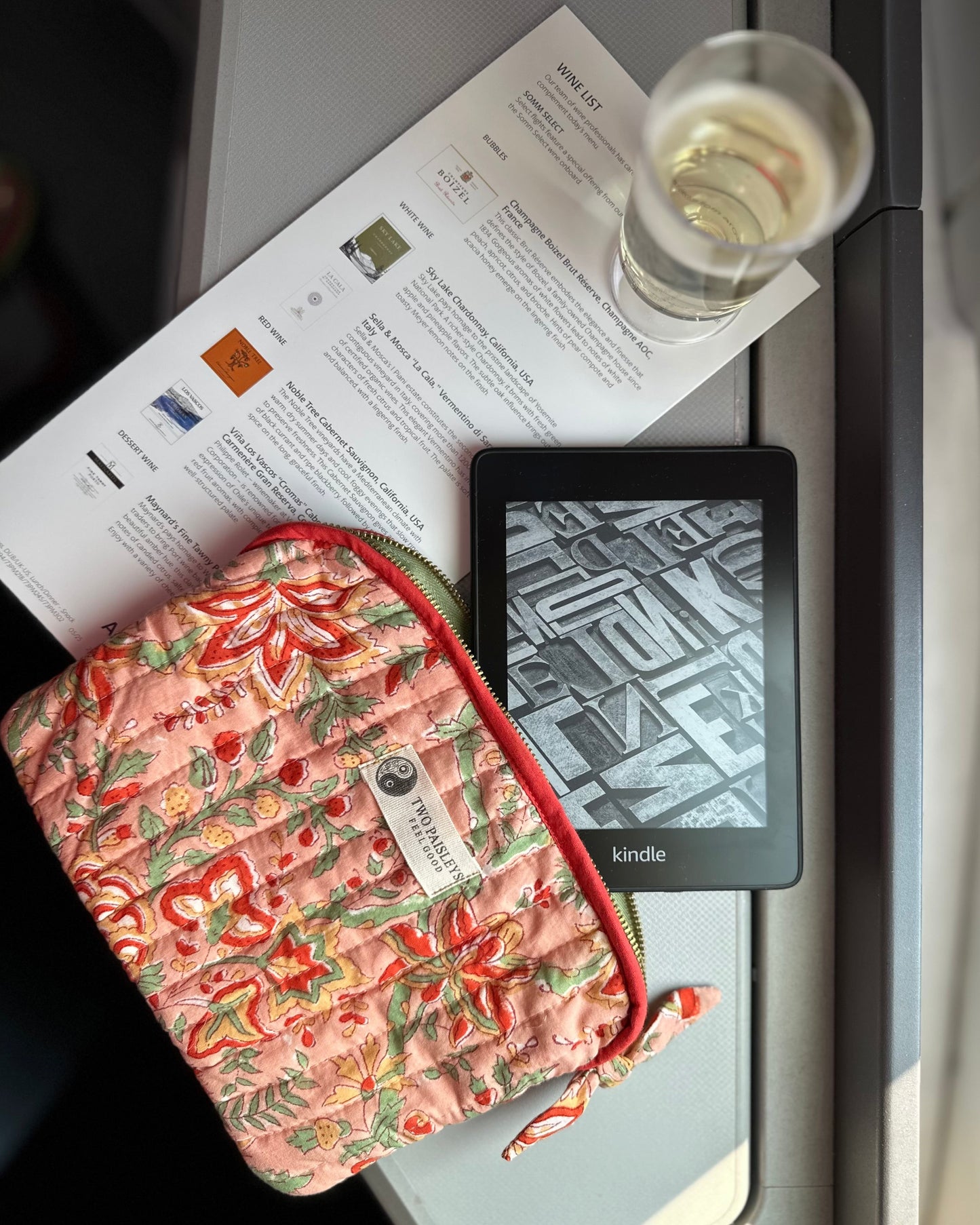 Floral-patterned pouch,Kindle device, and glass of water on a tray table.