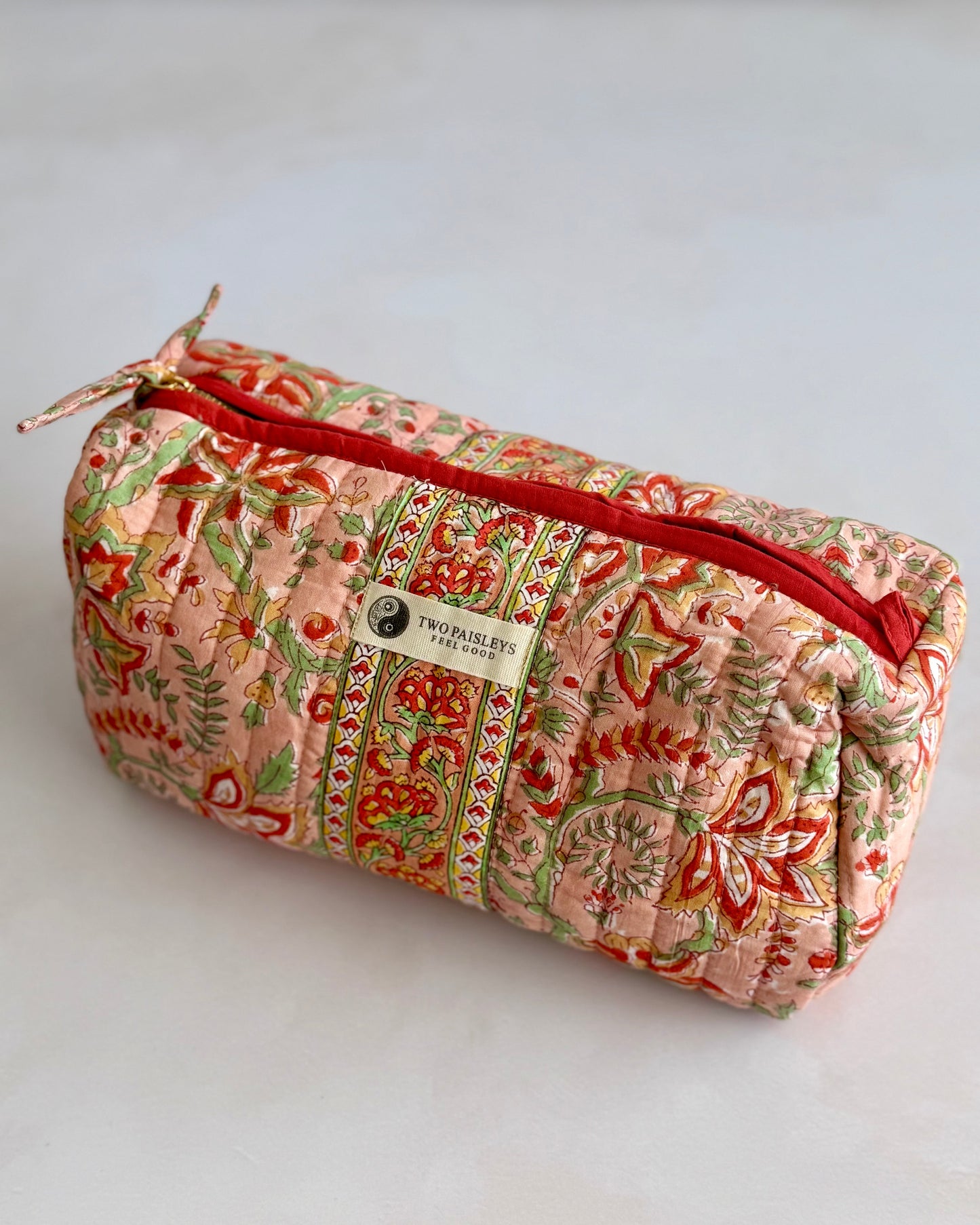 Quilted makeup bag with floral pattern and red zipper on a light gray background