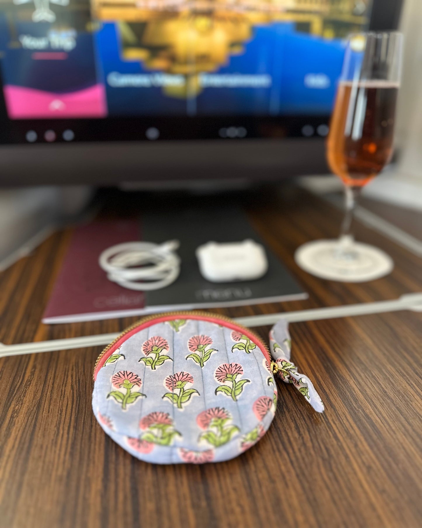 Round floral-jewellery AirPods ear bud patterned storage pouch on a wooden surface with a blurred background