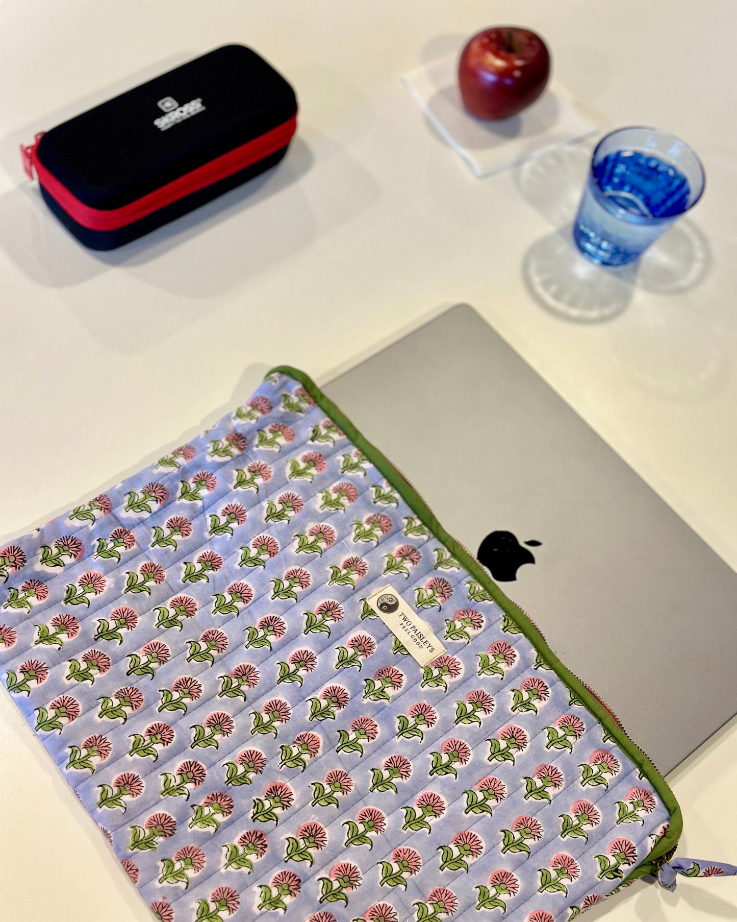 Floral patterned laptop sleeve on a laptop with an apple and pencil case in the background.