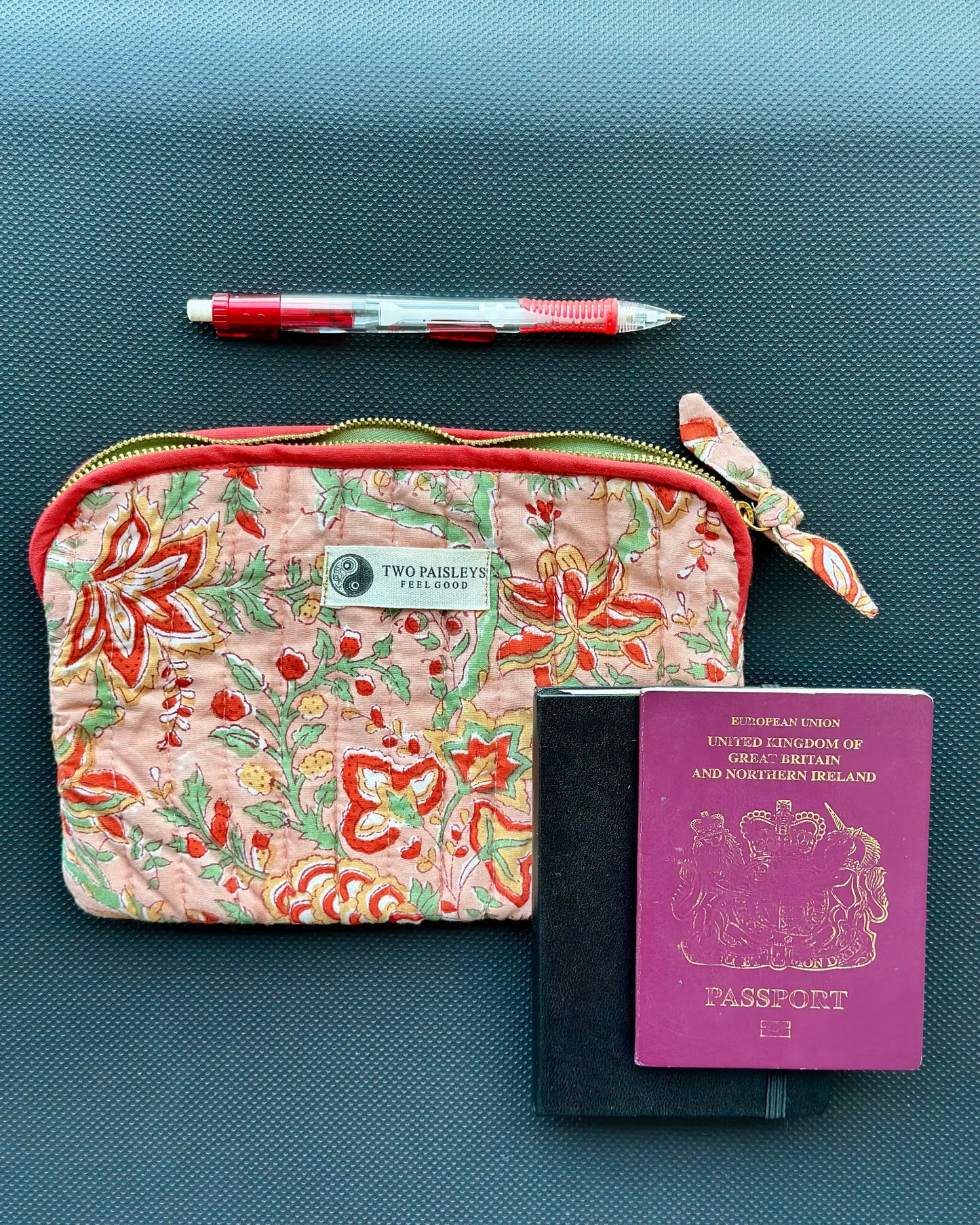 Floral-patterned pouch with a pen and passport on a textured surface