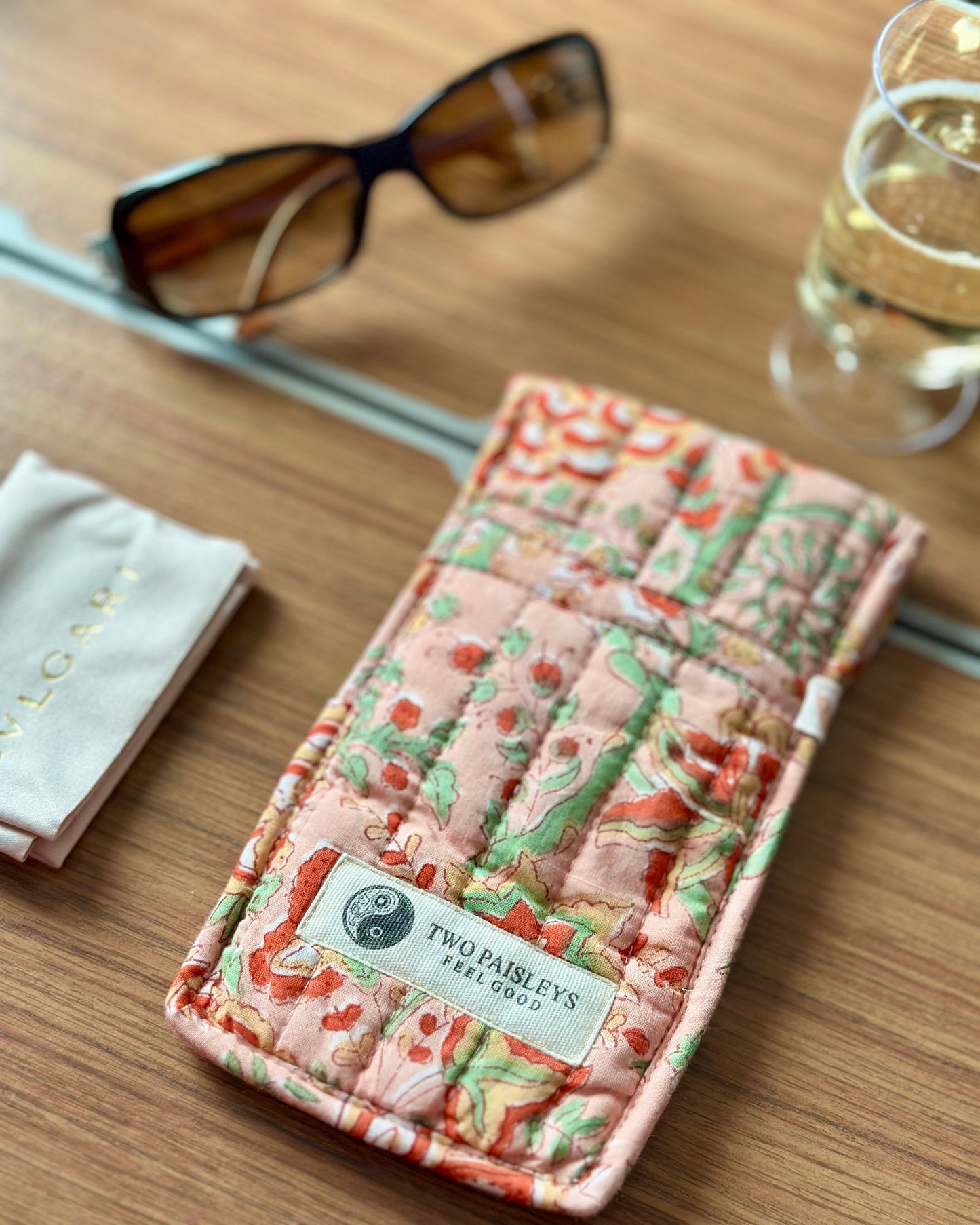 Patterned phone case with 'Two Paisleys' label on a wooden surface with sunglasses and a glass.