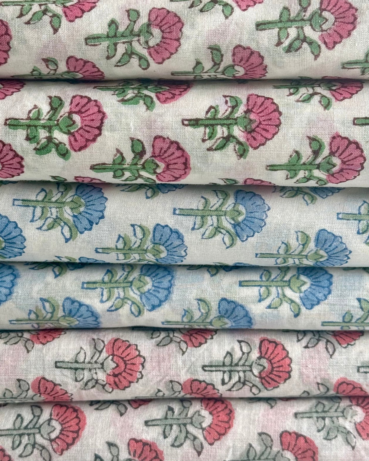 Stack of fabric with floral patterns in pink, blue, and green on a white background