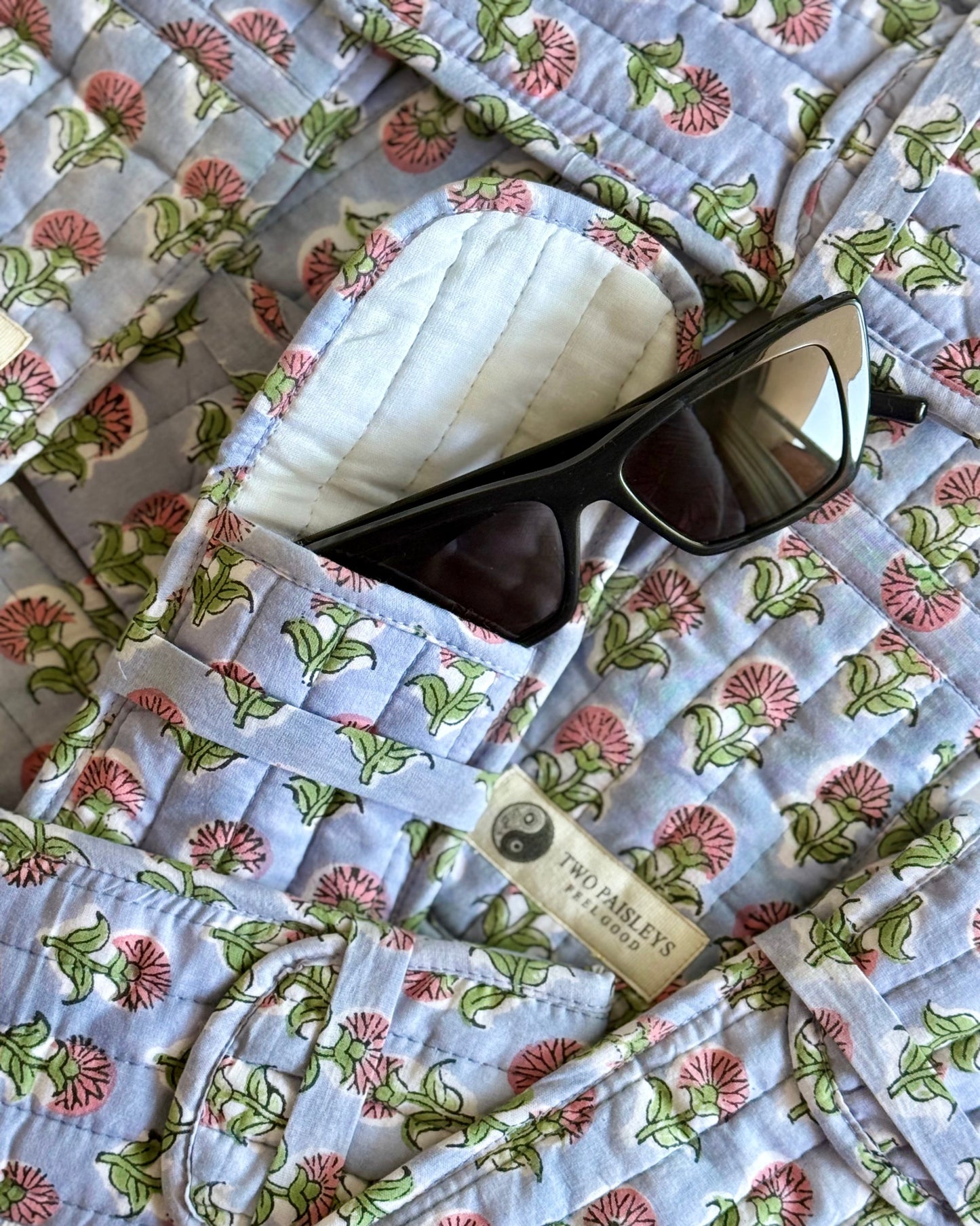 Floral-patterned glasses cases with sunglasses and a tag on a matching background