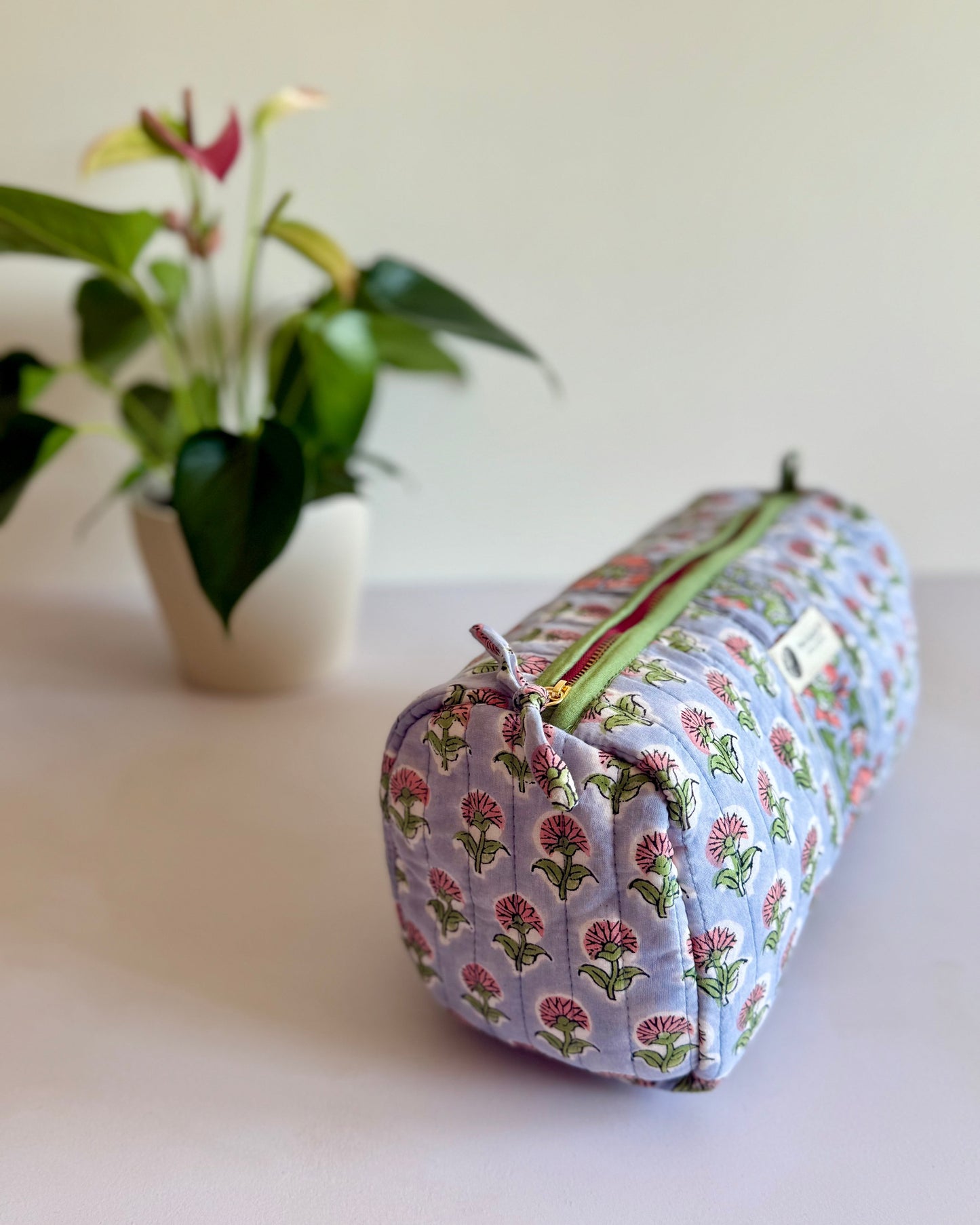 Floral-patterned cylindrical pouch on a light surface with a plant in the background