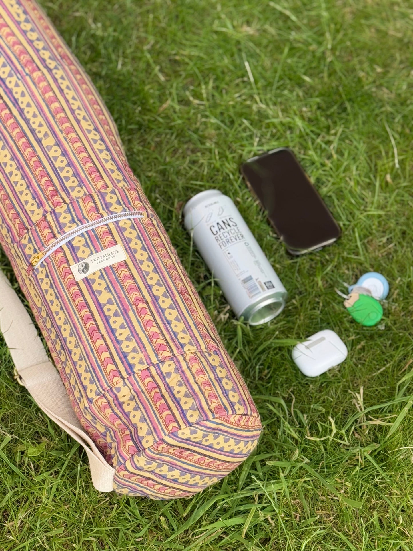 Colorful yoga mat with a can, phone, and small bottle on grass
