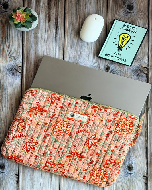 Floral-patterned laptop sleeve on a wooden surface with a mouse and card.