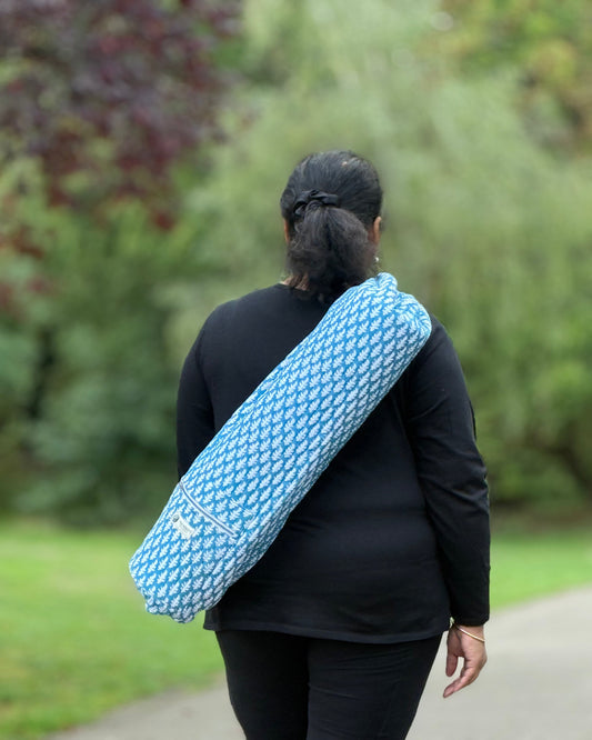 Woman carrying Blue Breeze cotton yoga mat cover with bright blue leafy print, crossbody with adjustable strap.