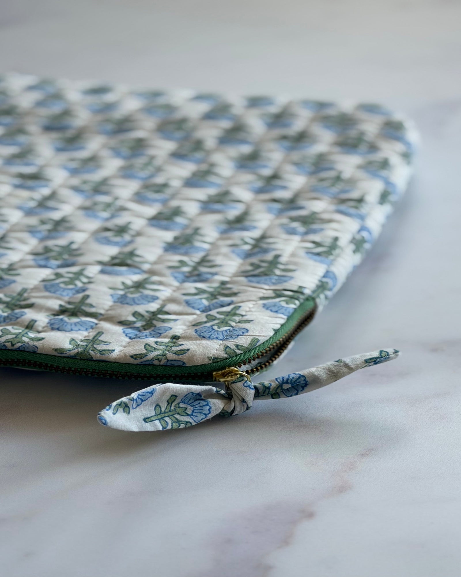 Close-up of the Blue Blossom hand block printed cotton fabric, quilted stitching and the contrast green zipper with bow tie detail.