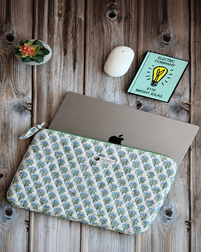 Blue & green floral-patterned laptop with laptop sleeve on a wooden desk with notebook and a mouse.