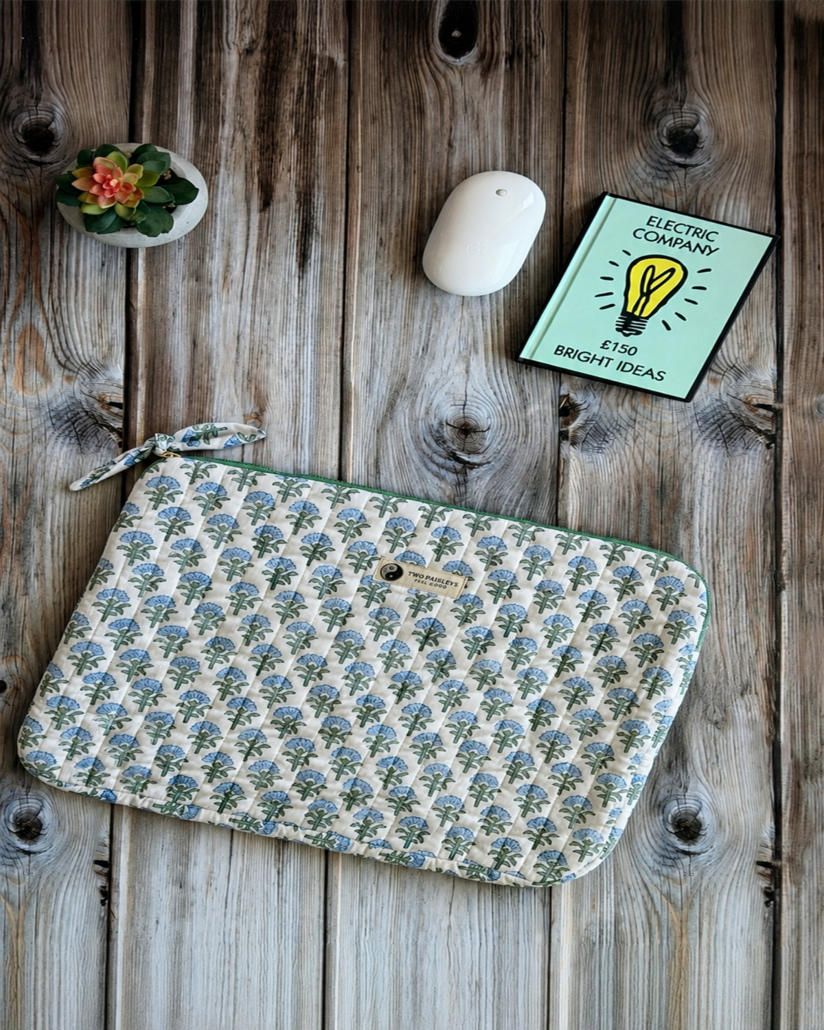 Blue & green floral pattern  laptop sleeve on a wooden desk with a plant and a wireless mouse.