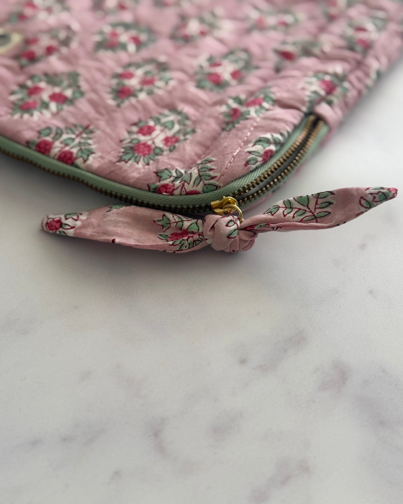 Close-up of the hand block printed blush floral cotton fabric with contrast green zipper of laptop sleeve