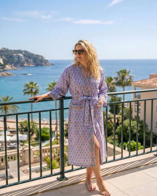 Woman in a lilac and pink floral  dressing gown  standing on a balcony with a scenic ocean view.