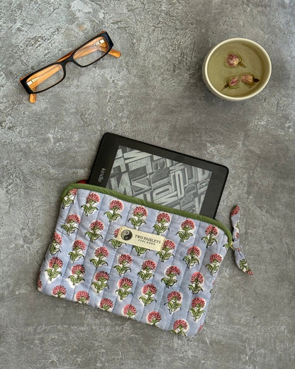 Floral-patterned quilted pouch with a kindle on a grey surface, accompanied by glasses and tea.