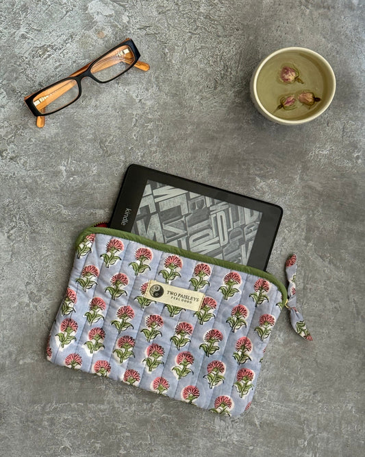 Floral-patterned quilted pouch with a kindle on a grey surface, accompanied by glasses and tea.