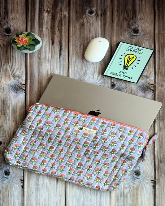 Laptop with a floral sleeve on a wooden surface with a plant and card.