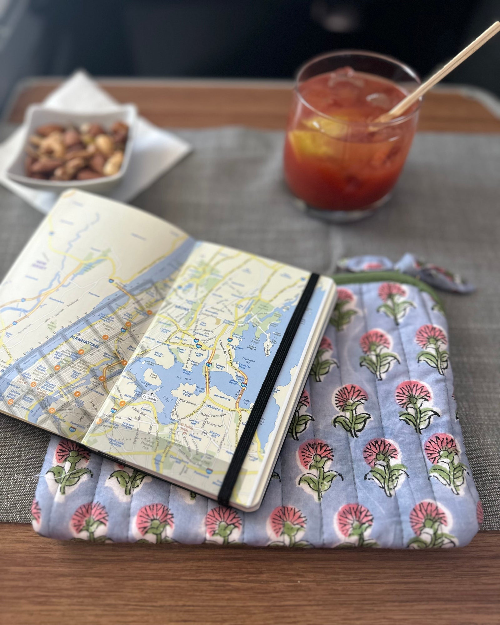 Notebook with map design on a floral cushion next to a drink on a table