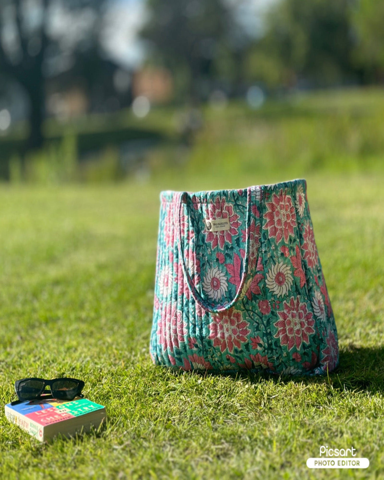Floral patterned bag on grass with sunglasses and book