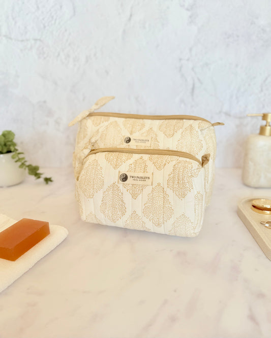 Beige with gold motif  toiletry bag on a bathroom counter with soap and dispenser.