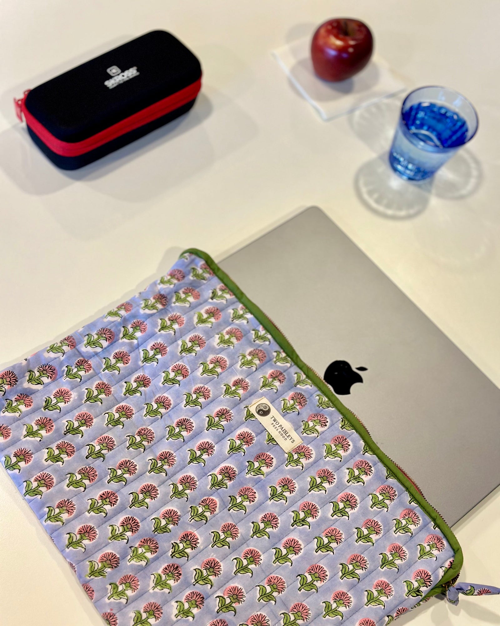 Floral patterned laptop sleeve on a laptop with an apple and pencil case in the background.