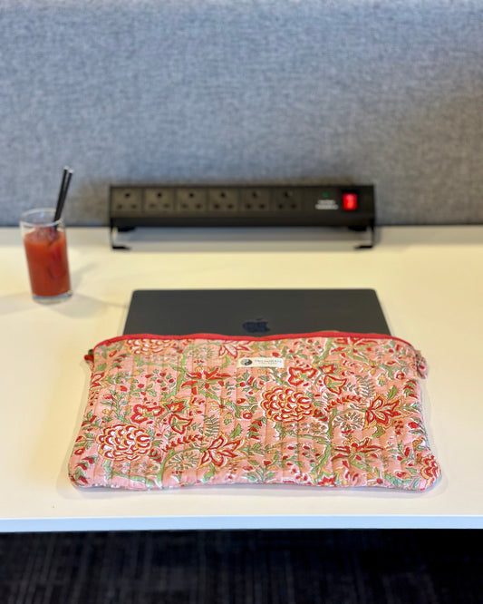 Floral-patterned pouch on a desk with a glass of juice and power strip in the background.