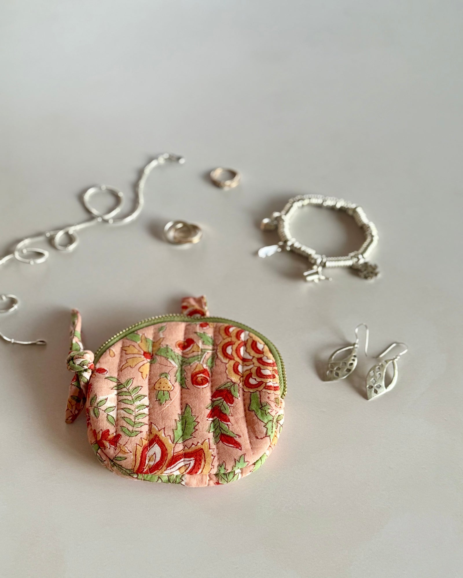 Small round floral-patterned pouch with silver jewelry on a light gray background