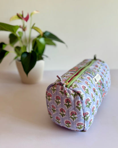 Floral-patterned cylindrical pouch on a light surface with a plant in the background