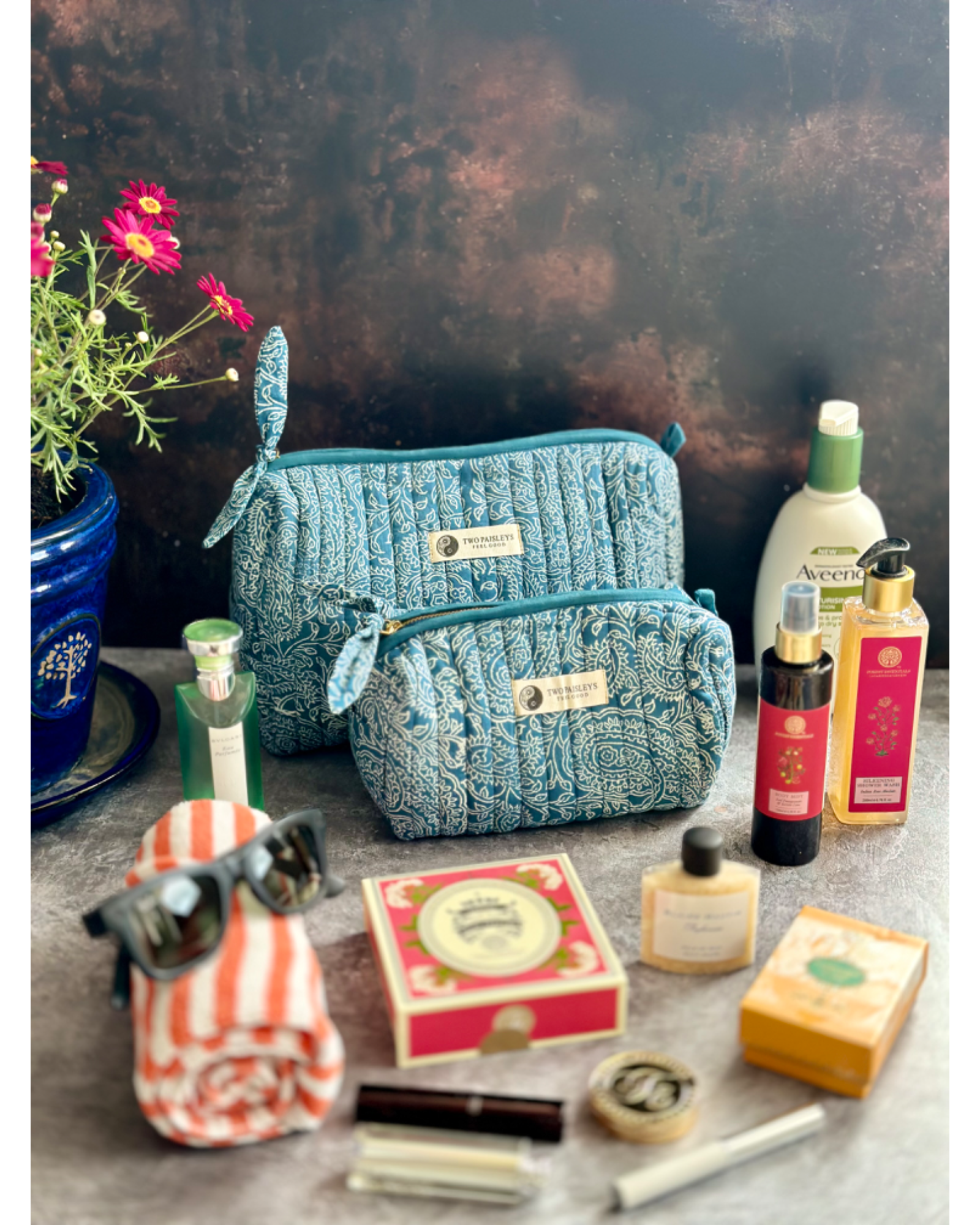A quilted wash bag with an indigo paisley print, displayed alongside various travel-sized toiletry items.