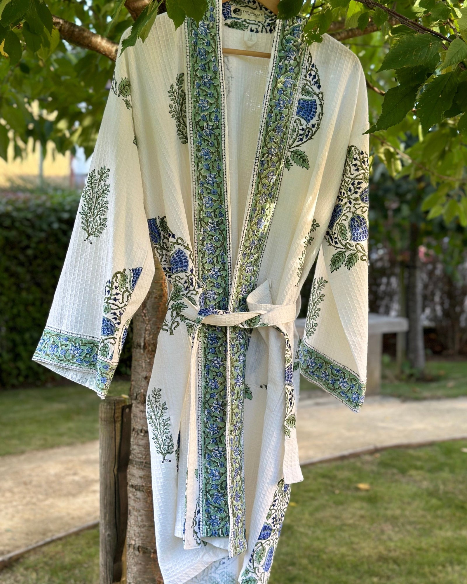 White kimono-style garment with green and blue patterns hanging on a tree branch outdoors.