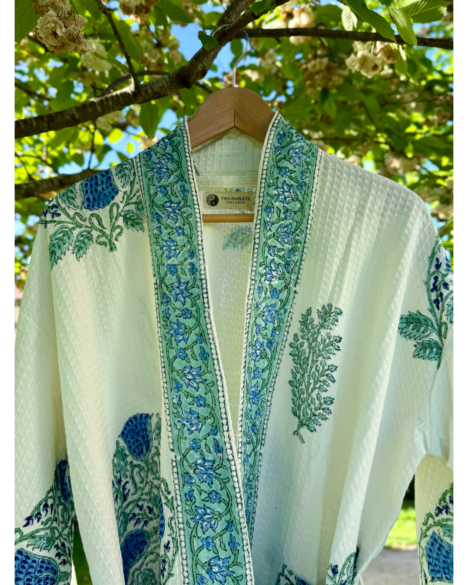 A white and blue block printed cotton bathrobe hanging on a hanger with foliage patterns