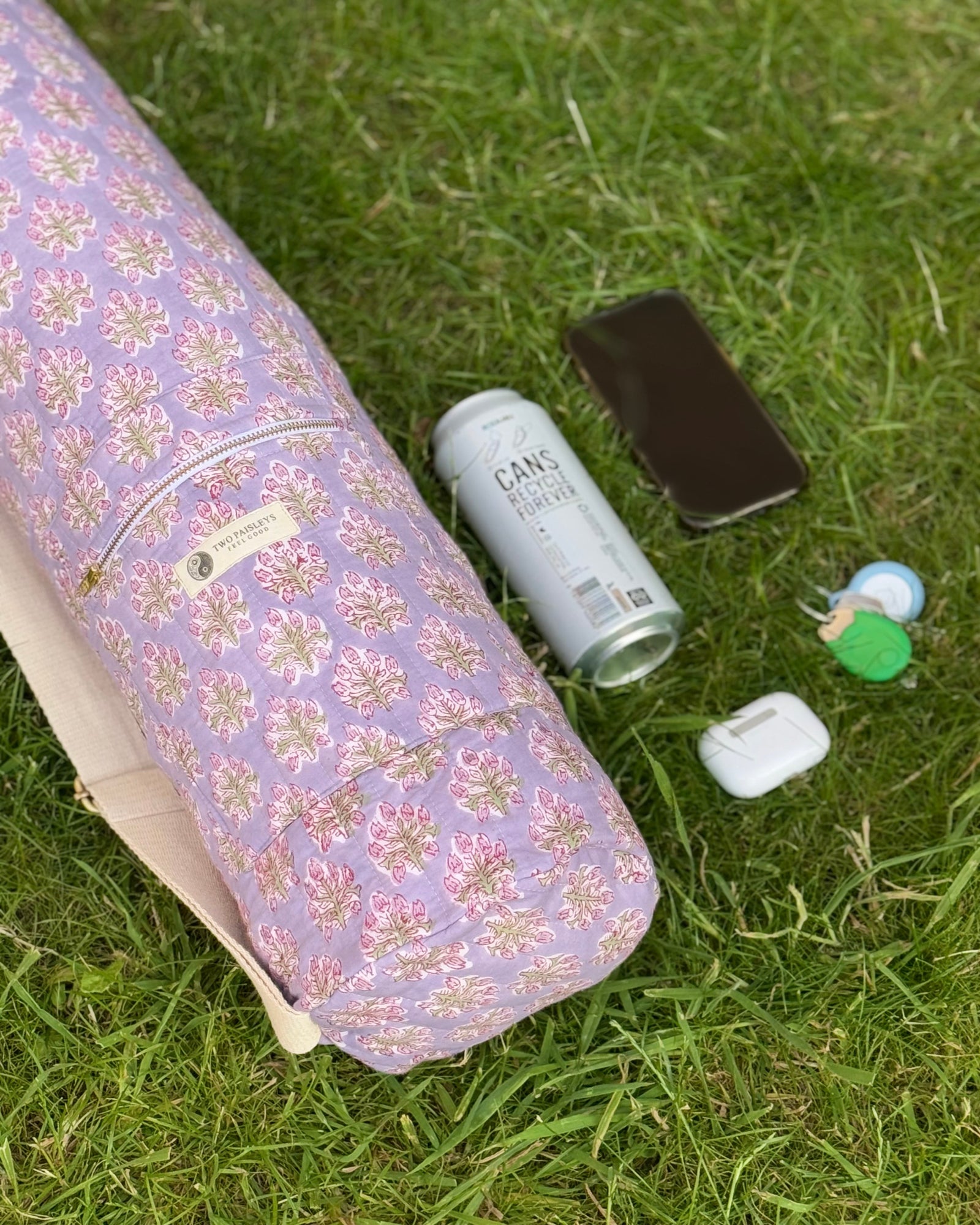 Floral-patterned yoga mat, can, phone, and earbuds on grass