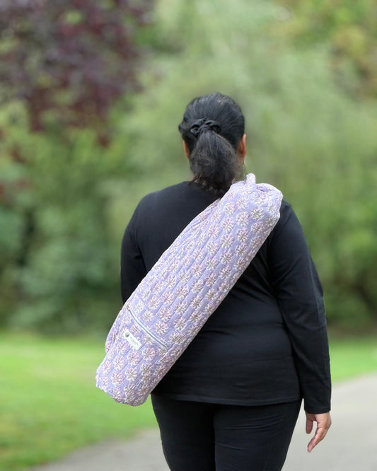 Person carrying a rolled-up yoga mat with a patterned cover outdoors.