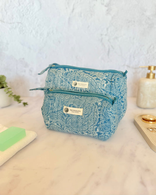 A quilted wash bag with an indigo paisley print, displayed alongside various travel-sized toiletry items.