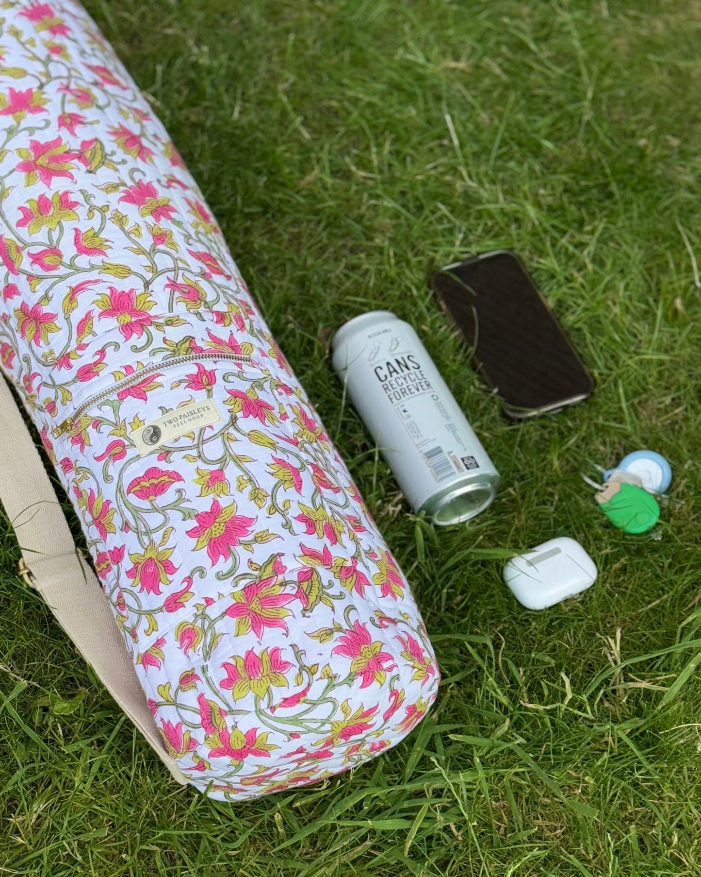 Floral-patterned yoga mat on grass with a can, phone, and other items.