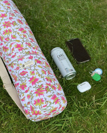 Floral-patterned yoga mat on grass with a can, phone, and other items.