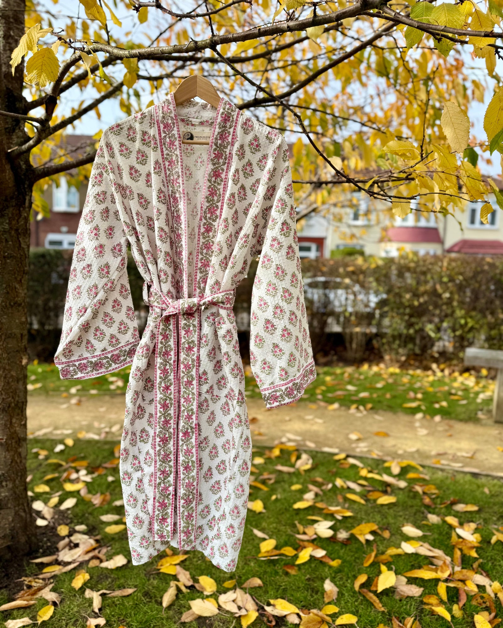 Full view of the 'Vintage Floral' pink and white hand block print waffle robe hanging in a garden.