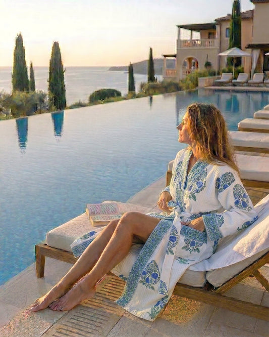Woman in a green and blue floral motifs on a white waffle robe sitting by an infinity pool with a scenic view.