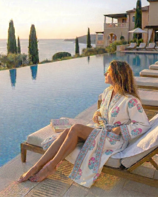 Woman in a pink & blue floral   white waffle robe relaxing by an infinity pool with a scenic view.