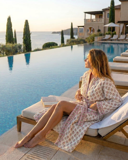 Woman in a pink floral waffle  robe sitting by an infinity pool with ocean view