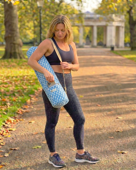 Woman in athletic wear holding a yoga mat bag on a path in a park.