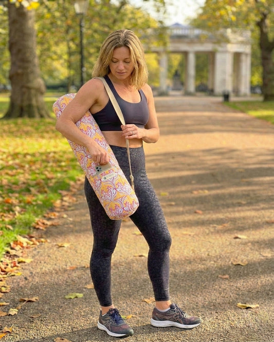 Woman holding a quilted yoga mat with a warm yellow floral design in a park setting