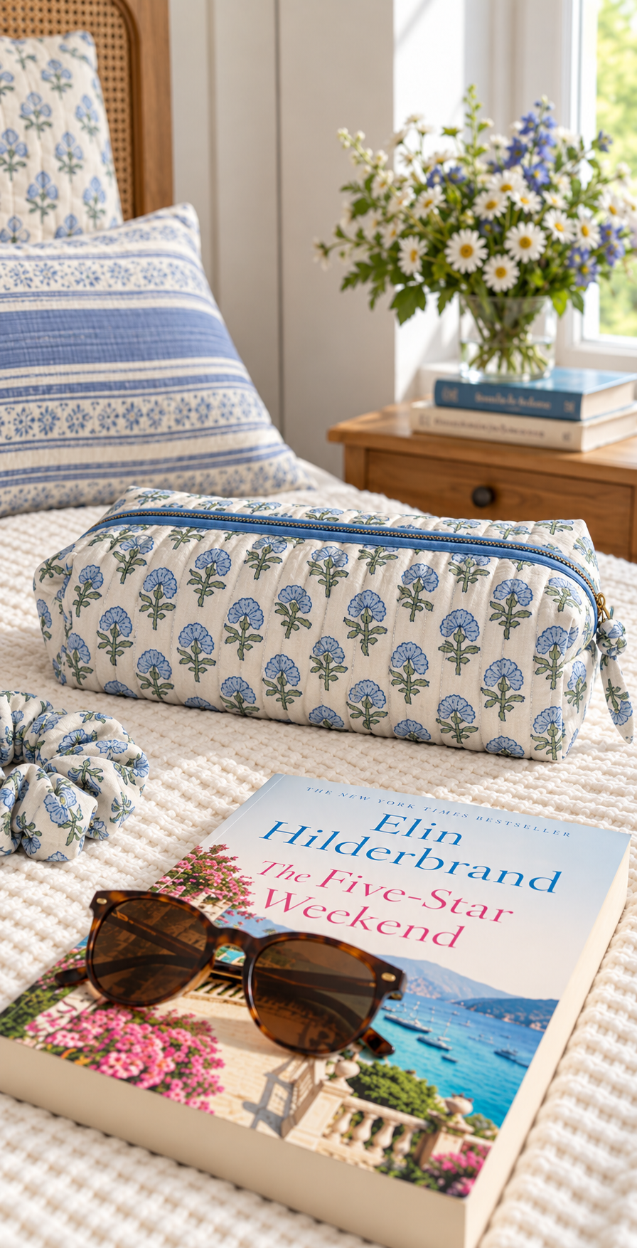 Two Paisleys Blue Blossom block printed quilted hair tools bag on a bed beside sunglasses and a book for weekend travel