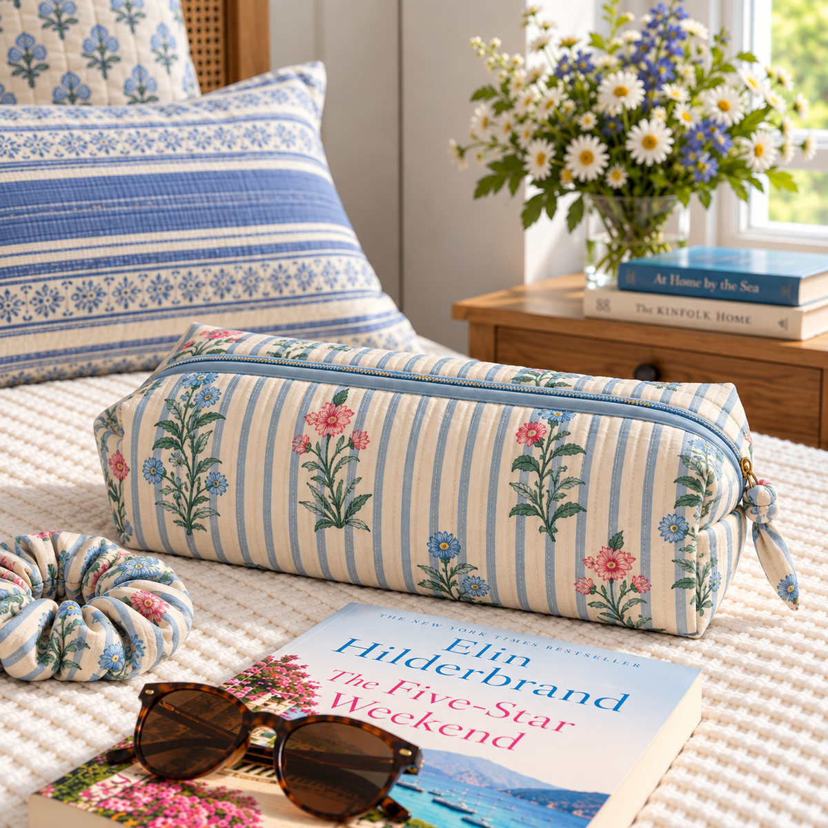 Two Paisleys Blue Stripe Floral hand block printed quilted hair tools bag on a bed beside sunglasses and a book for weekend travel