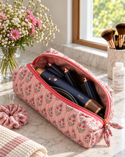 Open Two Paisleys pink quilted cotton hair accessories travel bag holding a Dyson Airwrap multi-styler and styling attachments on a vanity unit.