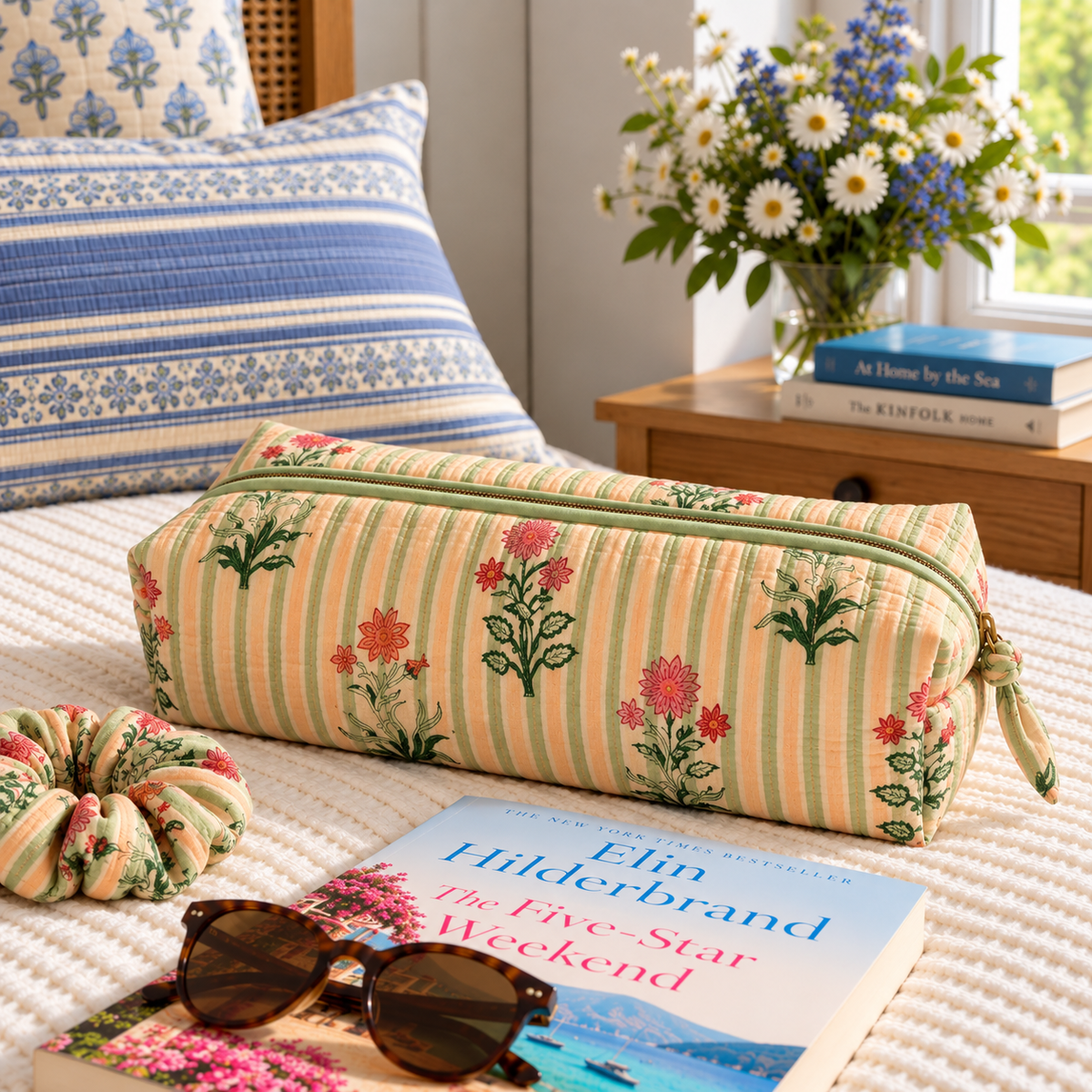 Two Paisleys Green Stripe Floral hand block printed quilted hair tools bag on a bed beside sunglasses and a book for weekend travel