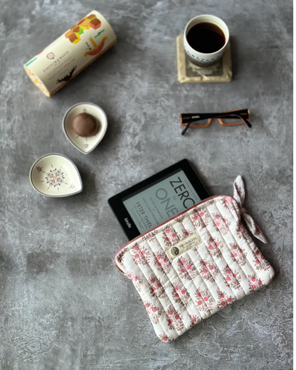 Hand block printed quilted cotton Kindle cover by Two Paisleys in a pink & green floral print along side a cup of tea & some biscuits and reading glasses.